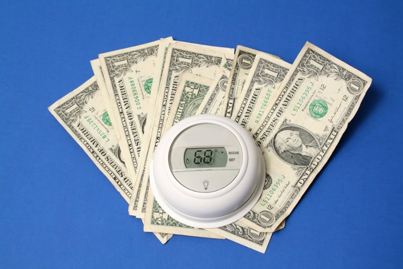 Spring Money-Saving Tips. Thermostat on a pile of money.