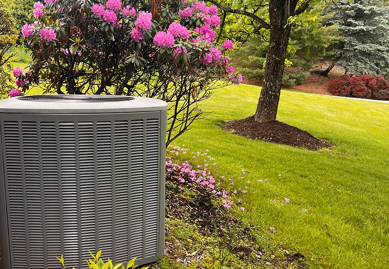 An outdoor central air conditioning condenser unit integrated into a beautifully landscaped backyard.