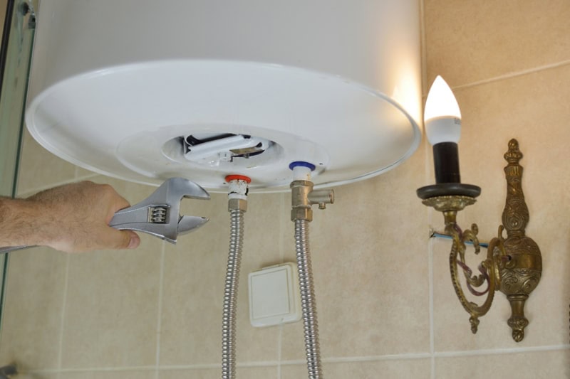 Everything You Need to Know About Boilers. Repairing a boiler with a wrench in a bathroom.