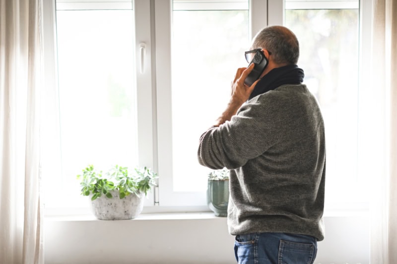 Why Won’t My Furnace Stop Running? Photo of a man looking out his window while talking on his phone.