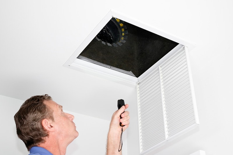 Man looking into air vent with flashlight.